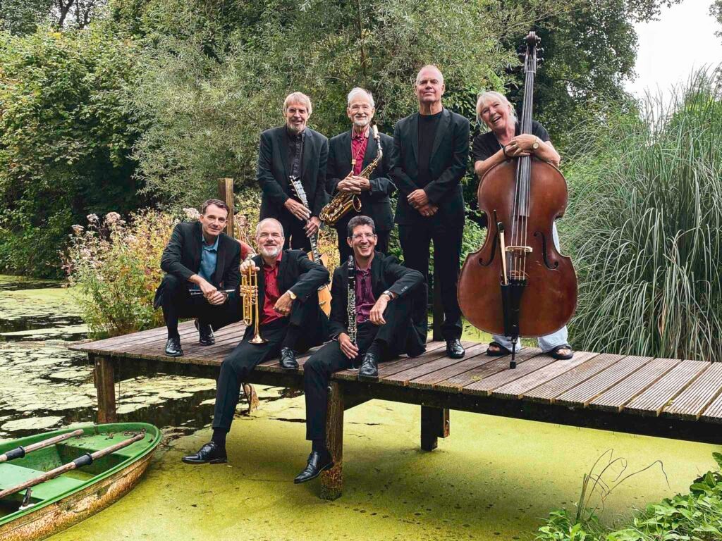 Die Barrelhouse Jazzband im Jahr 2024 auf einem Steg in Neu-Isenburg, eingebettet in eine grüne Landschaft. Dieses Bild fängt die zeitlose Eleganz und Spielfreude der Band ein, die seit über 70 Jahren ihren unverkennbaren Mix aus klassischem Jazz, frühem Swing, New-Orleans-Renaissance und karibischen Rhythmen auf die Bühne bringt.